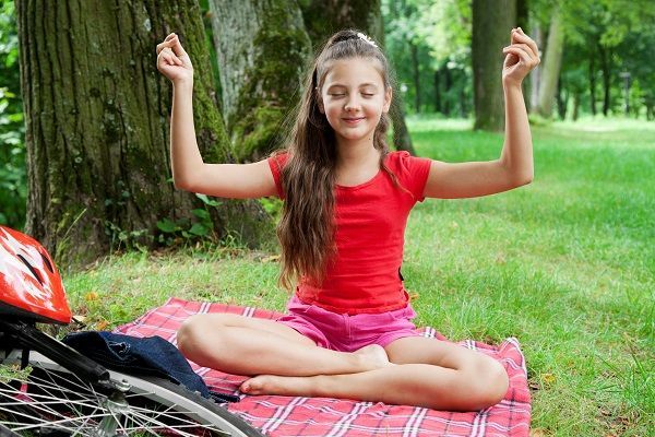 Une jeune fille dans la position du lotus assise sur l'herbe