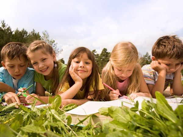 Des enfants allongés dans l'herbe sourient et se penchent sur des cahiers