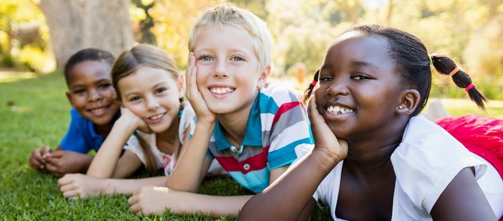 Des enfants accoudés dans l'herbe sourient en regardant l'objectif