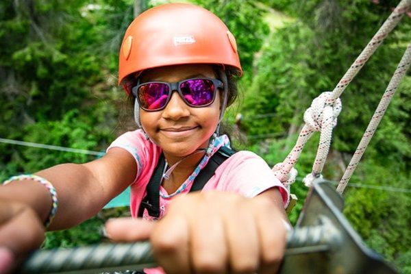 Un enfant avec un casque et des lunettes se tient au sommet d'un parcours aventure