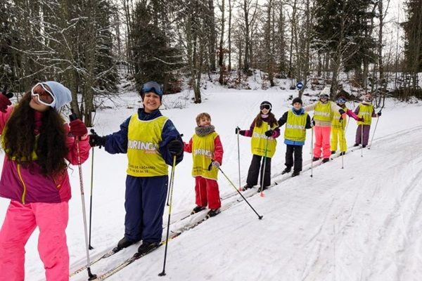 Des enfants en file indienne font du ski de fond dans la neige avec des animatrices