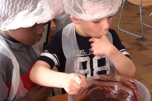 Des enfants coiffés d'une charlotte préparent un gâteau au chocolat