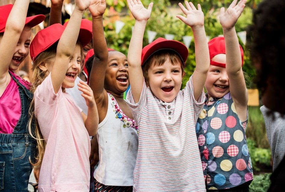 Un groupe d'enfants portant des casquettes rouges lève la main en souriant