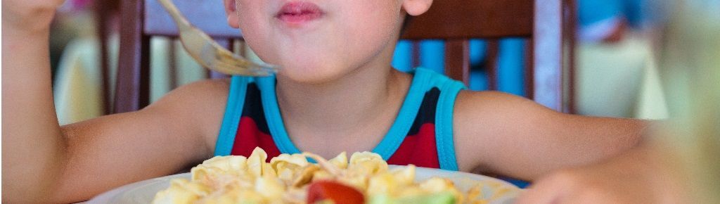 Un enfant mange une assiette de pâtes avec des légumes