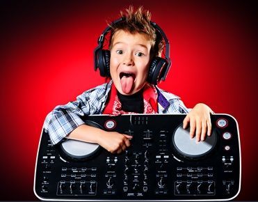 Un enfant qui tire la langue porte un casque audio et pose les mains sur une platine de mixage