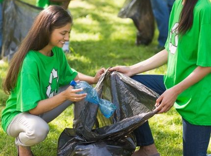Des jeunes filles en t-shirt vert ramassent des déchets avec le sourire