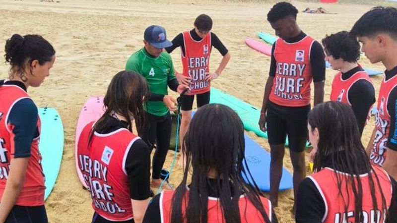 Un groupe de jeune d'une école de surf écoute les consignes d'un moniteur sur la plage