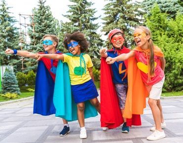 Des enfants costumés en super-héros sourient et tendent le bras