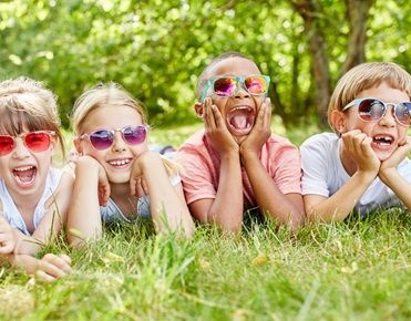 Des enfants allongés dans l'herbe sourient et portent des lunettes de soleil en ayant l'air heureux.
