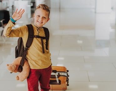 Un enfant portant un sac à dos et une valise dit au revoir avant de partir en colonies de vacances