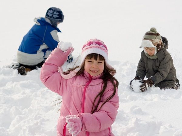 Trois enfants vêtus de vêtements de neige jouent à faire des boules de neige