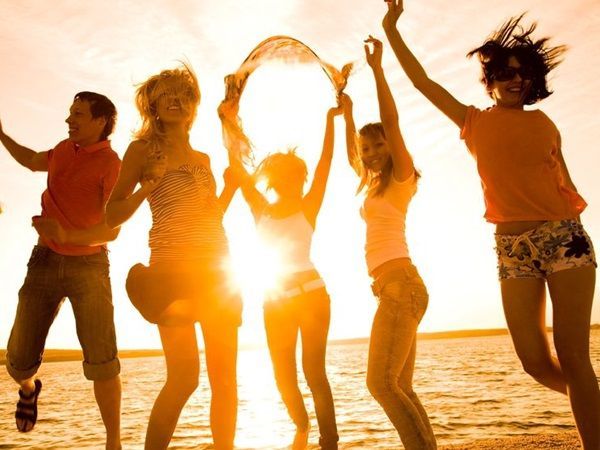 Un groupe d'adolescents saute en l'air à contre jour sur une plage en été