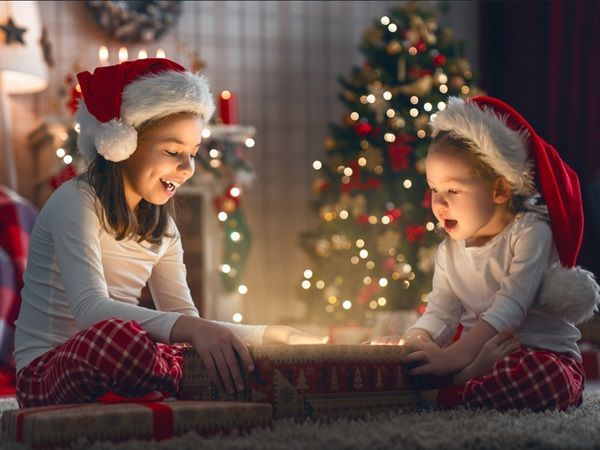 Deux enfants coiffés d'un bonnet de Noël ouvrent un cadeau avec un sapin en fond