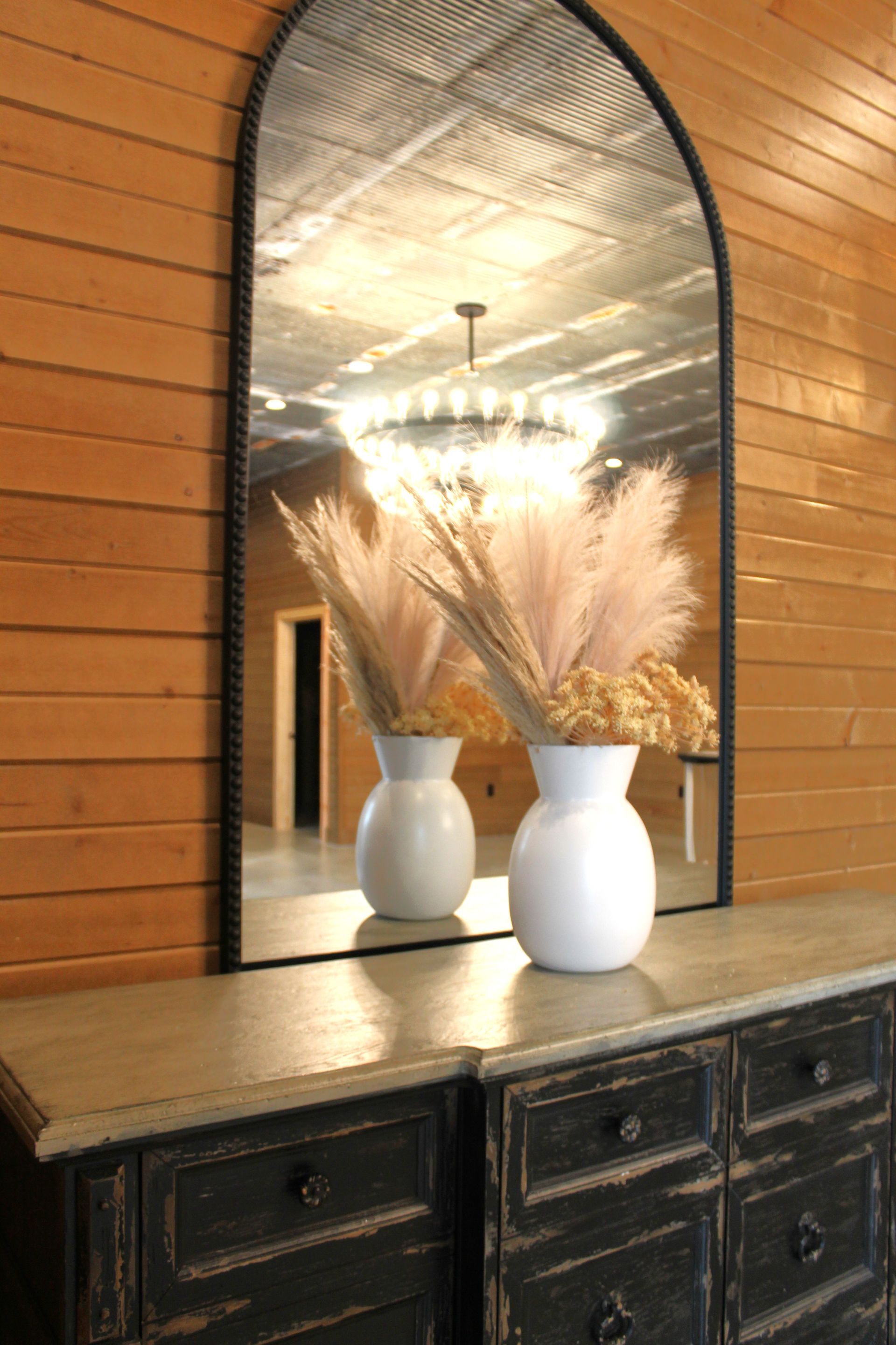 A large mirror with two vases of flowers in front of it.