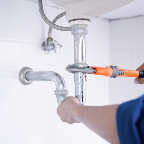 A man is fixing a sink pipe with a wrench.