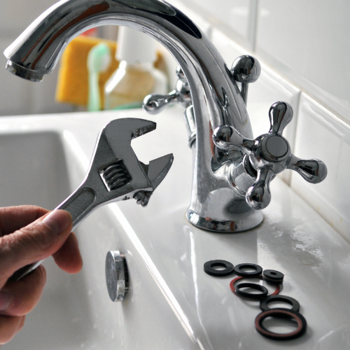 A person is fixing a faucet with a wrench