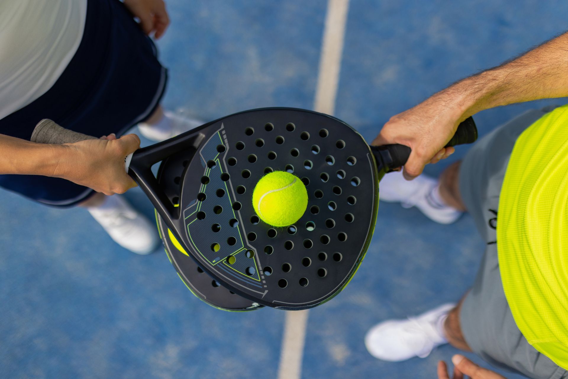 Due persone tengono in mano delle racchette da paddle con una palla sopra, su un campo blu.
