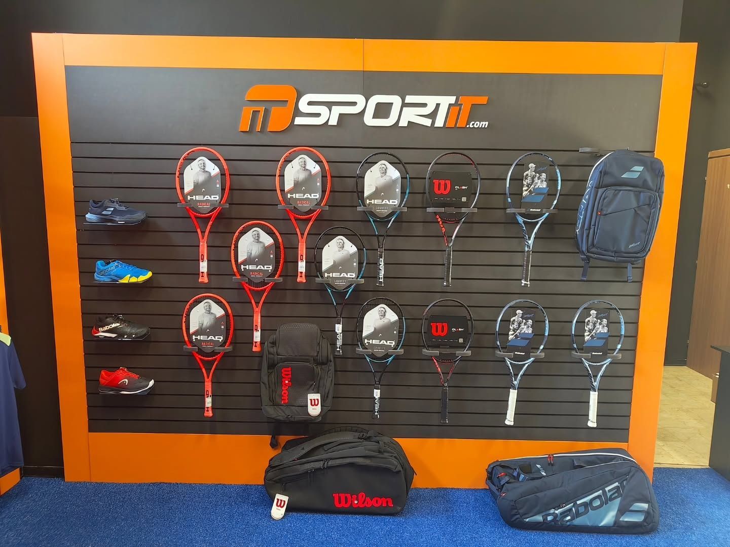 Racchette da tennis, scarpe e borse esposte sulla parete di un negozio con il logo "MD SPORT".