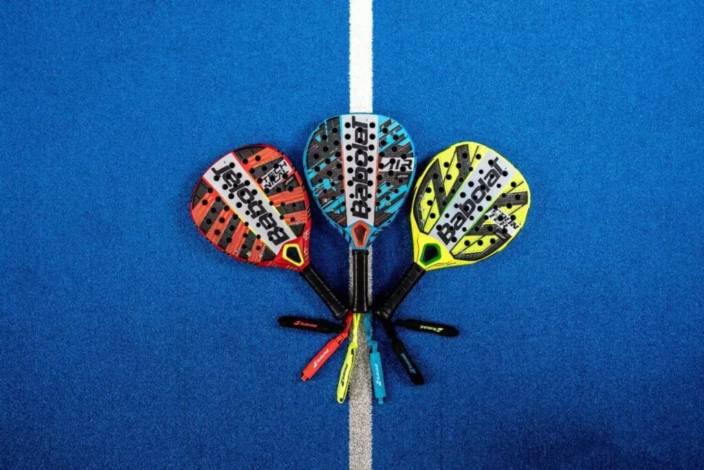 Tre racchette da paddle colorate su un campo blu con una linea bianca.