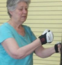 Woman in blue shirt boxing with gloves near a tan wall.