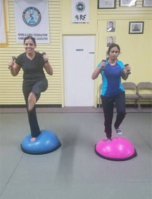Two people exercising on balance balls, holding dumbbells in a gym. Two people exercising on balance balls, holding dumbbells in a gym.
