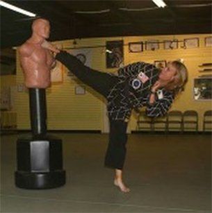 Woman in martial arts uniform kicking a heavy bag. Woman in martial arts uniform kicking a heavy bag.