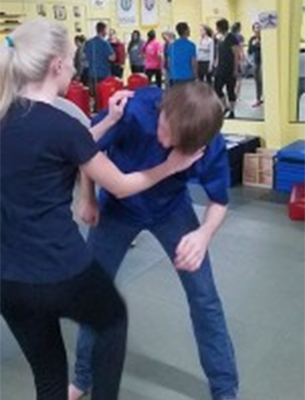 Woman in black shirt and leggings practices a self-defense move on a person in blue shirt and jeans.
