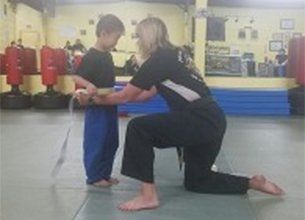 A woman kneels, adjusting a boy's belt in a martial arts studio. A woman kneels, adjusting a boy's belt in a martial arts studio.