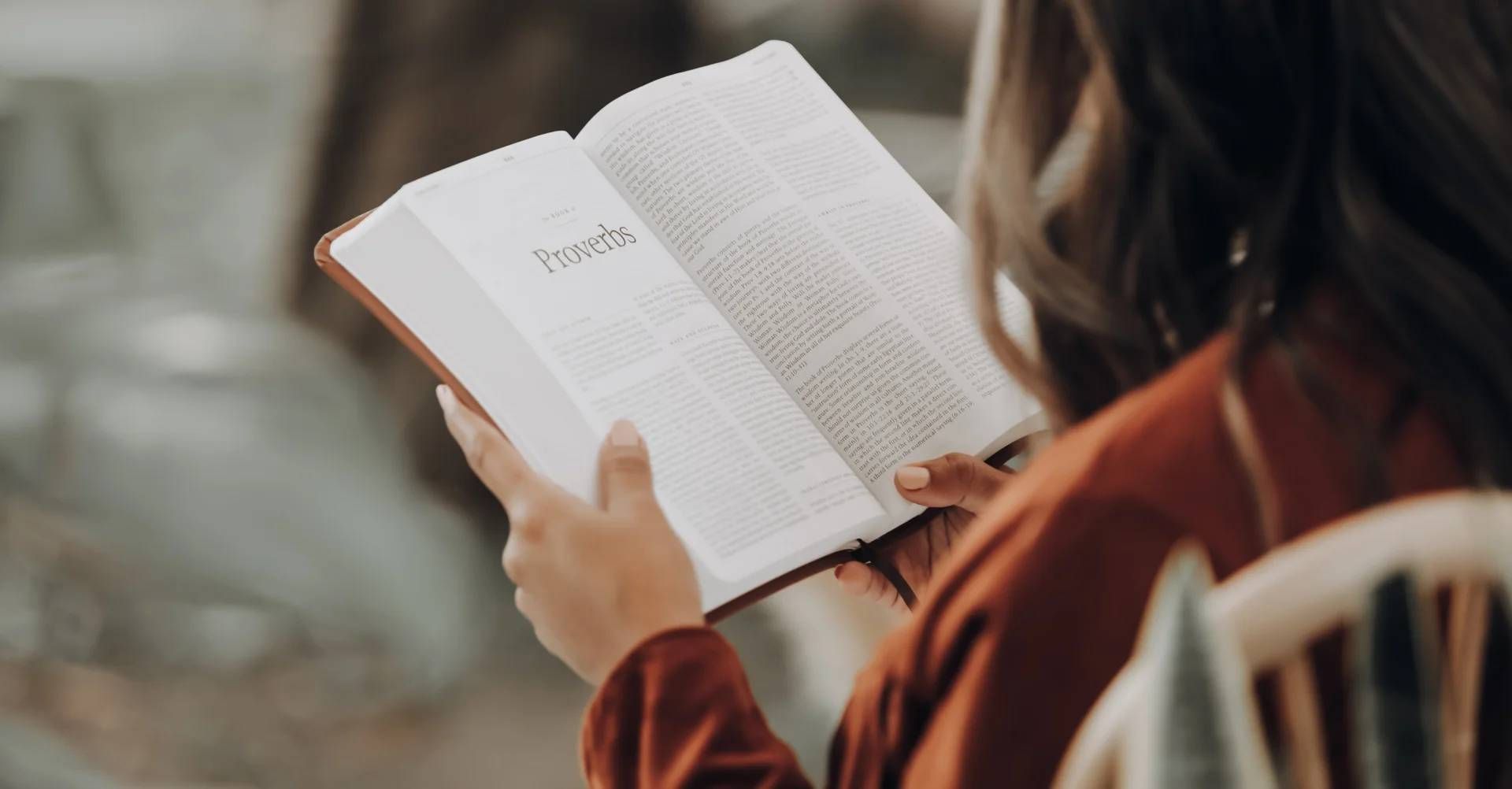 A woman is sitting in a chair reading a bible.