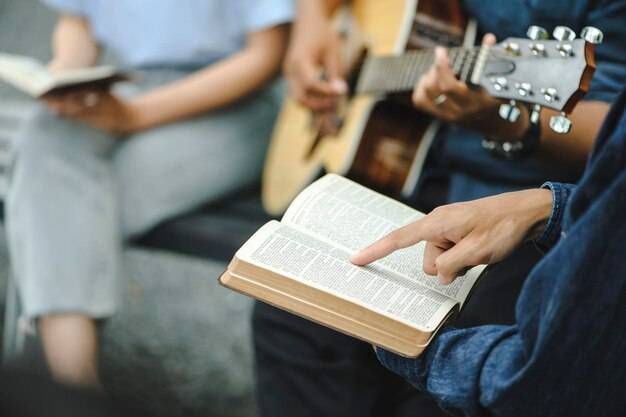 A person is pointing at a bible while another person plays a guitar.