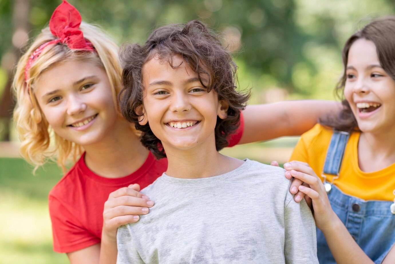 A boy and two girls are standing next to each other in a park.