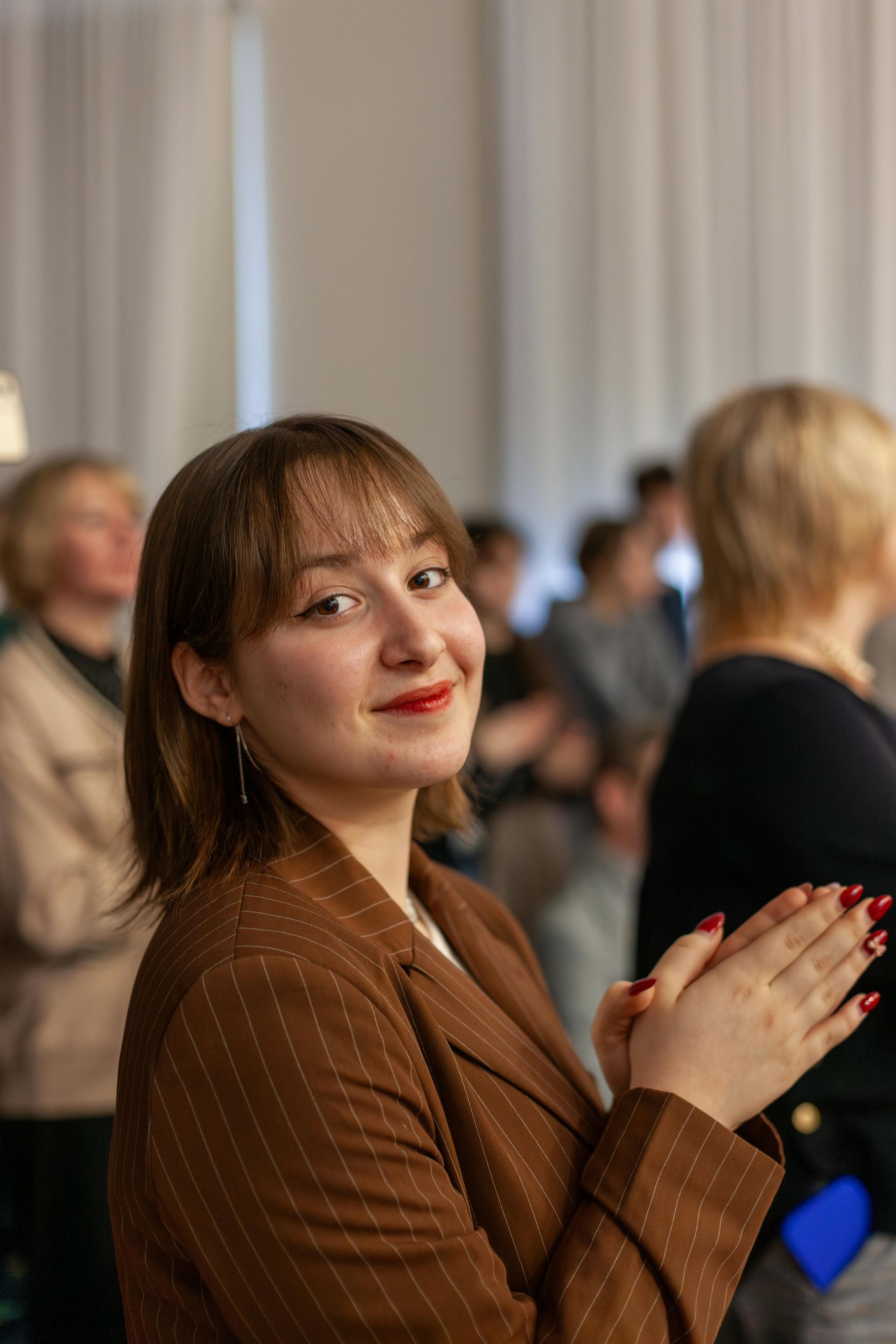 A woman in a brown suit is clapping her hands in a crowd of people.