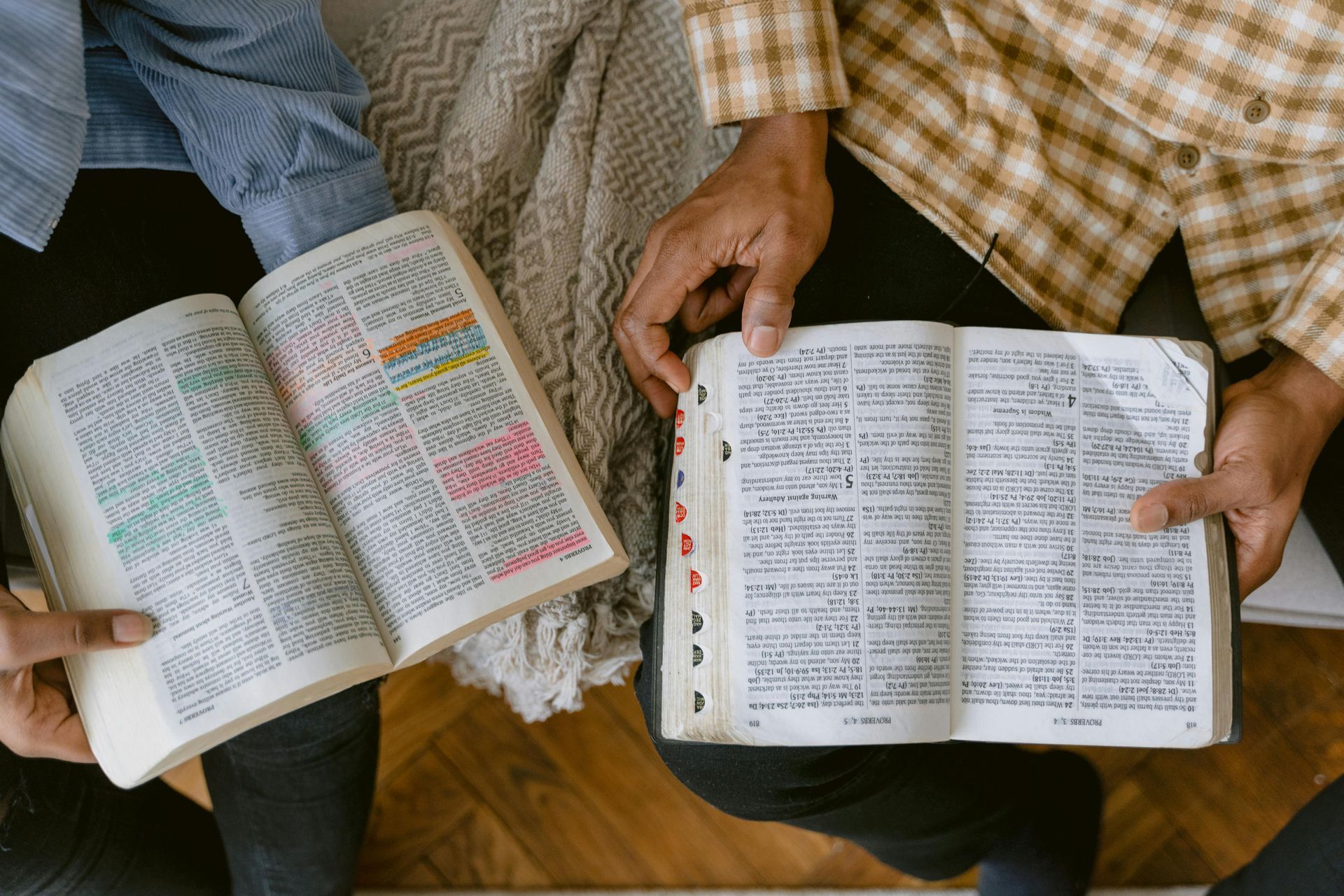Two people are sitting on a couch reading bible books.