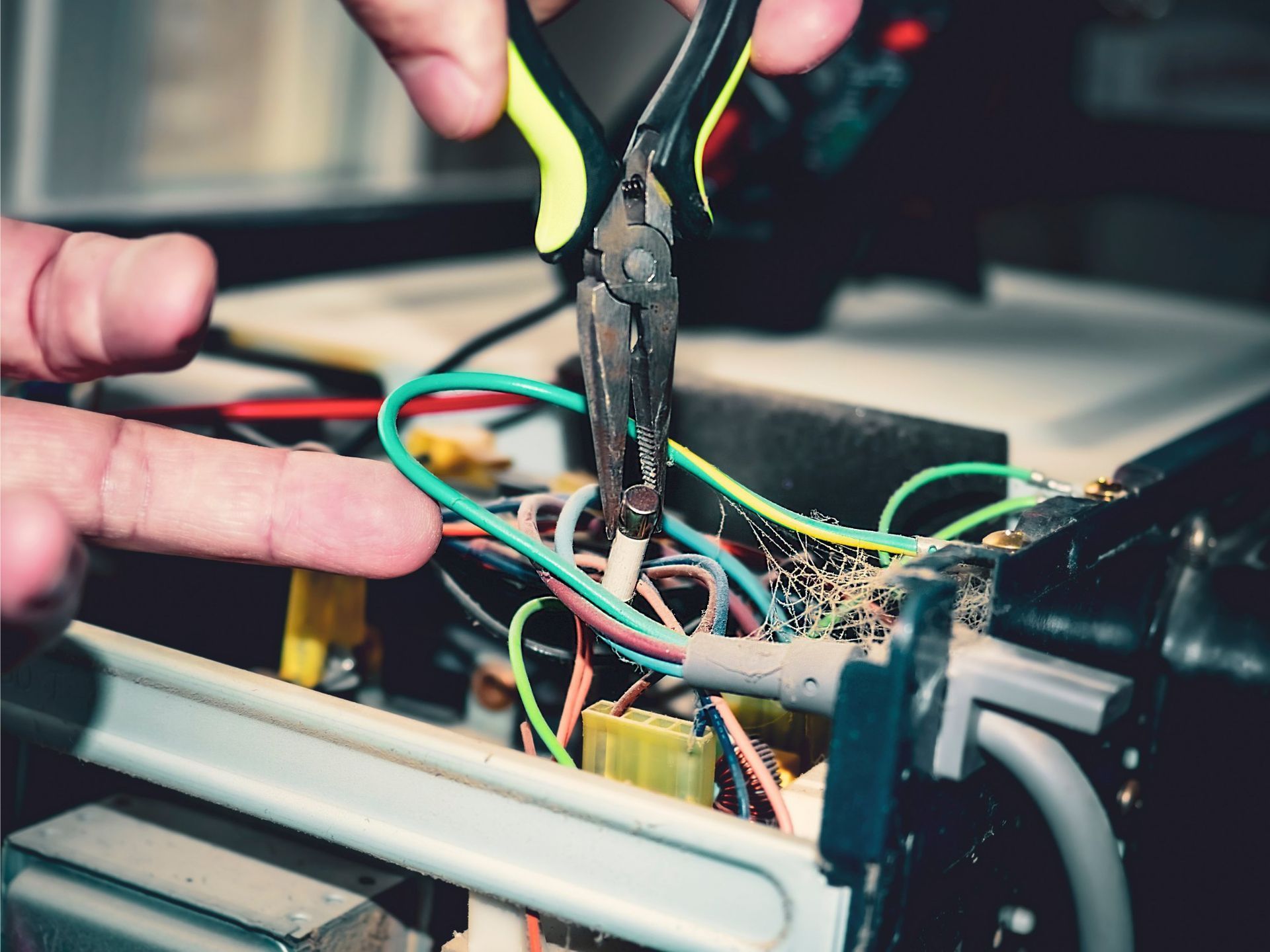 A person using pliers to cut a wire in a cluttered electronic device; green and yellow wires are visible.
