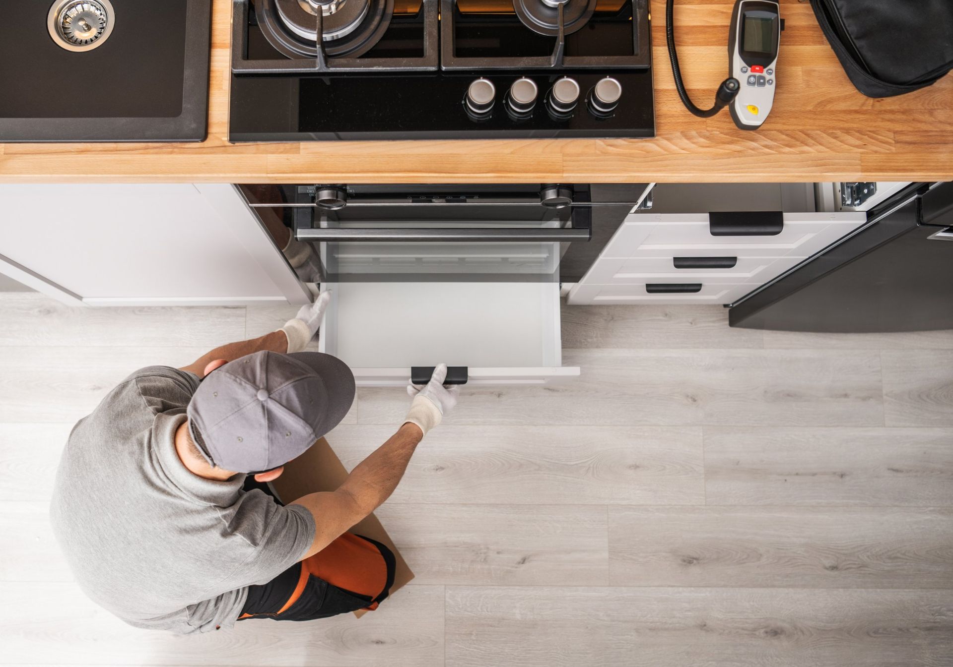 A person wearing gloves and a cap installs a drawer in a kitchen.