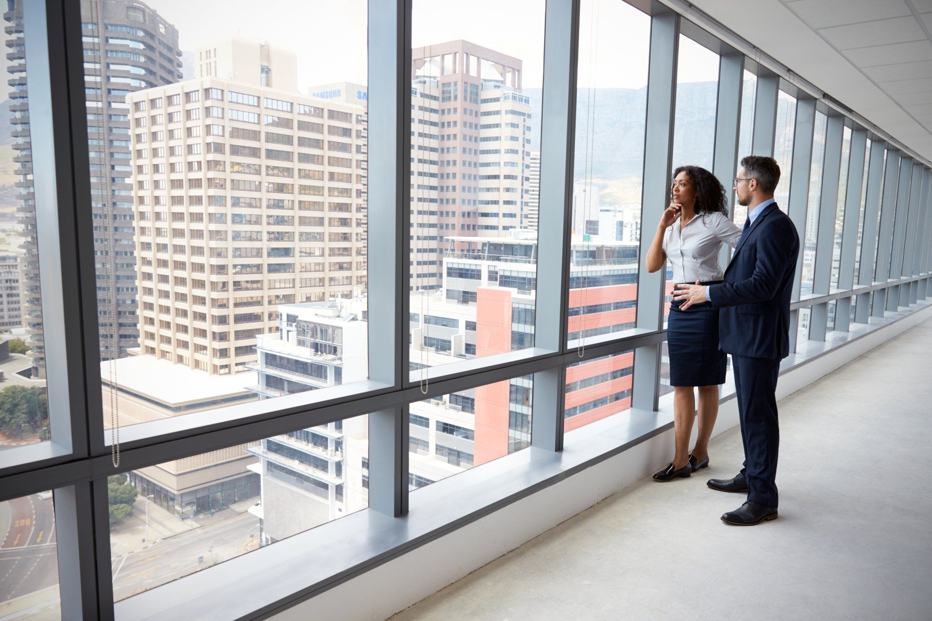 A man and a woman are looking out of a window in an office building.