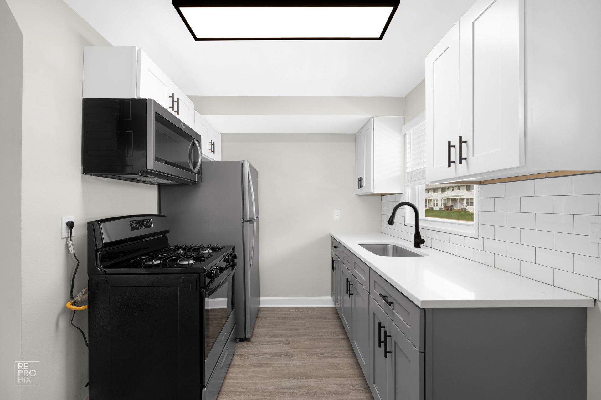 Small, modern kitchen with gray and white cabinets, appliances, and wood-look floors.