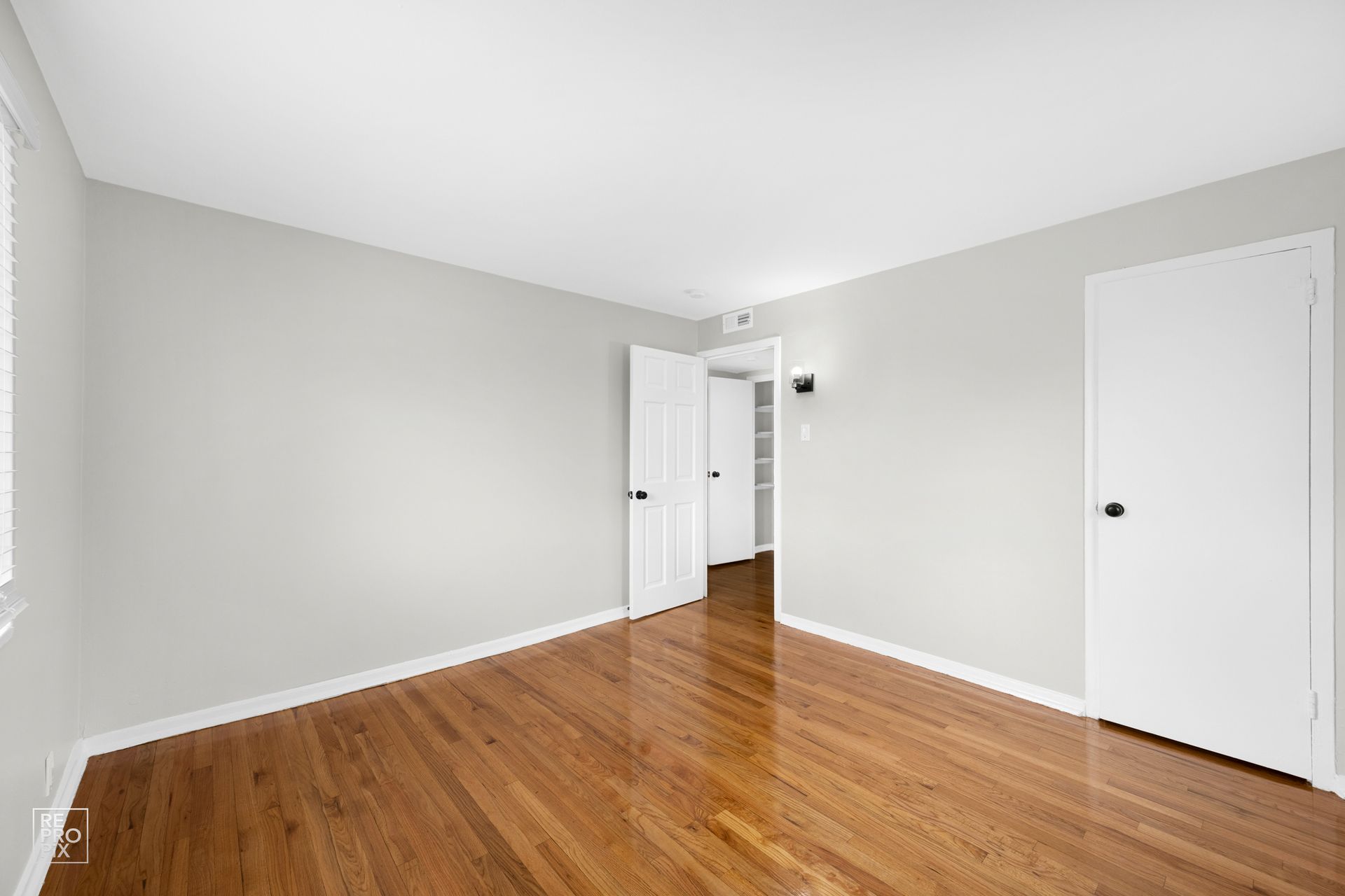 Empty room with hardwood floors, white walls, and closed doors.