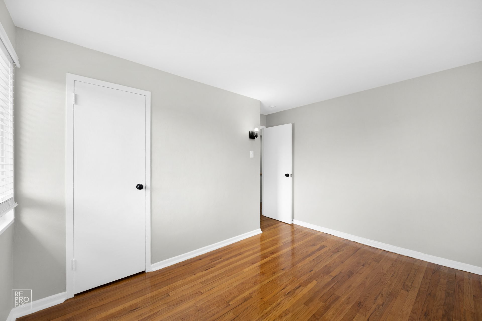 Empty room with hardwood floor, white doors, gray walls, and window.