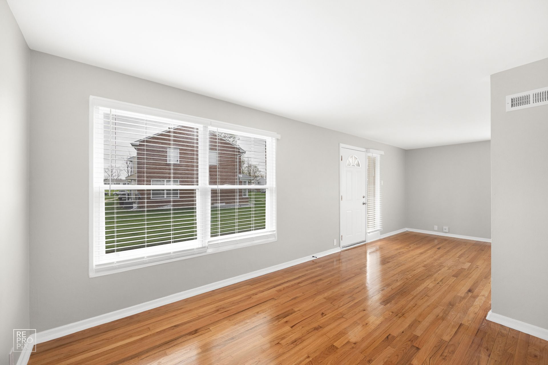 Empty living room with hardwood floors, large window, and white walls.