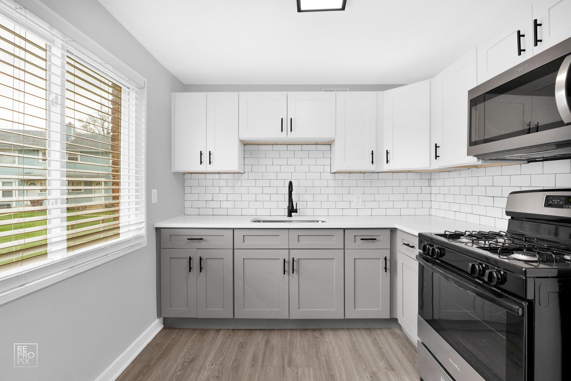 Modern kitchen with white and gray cabinets, stainless steel appliances, and a window.