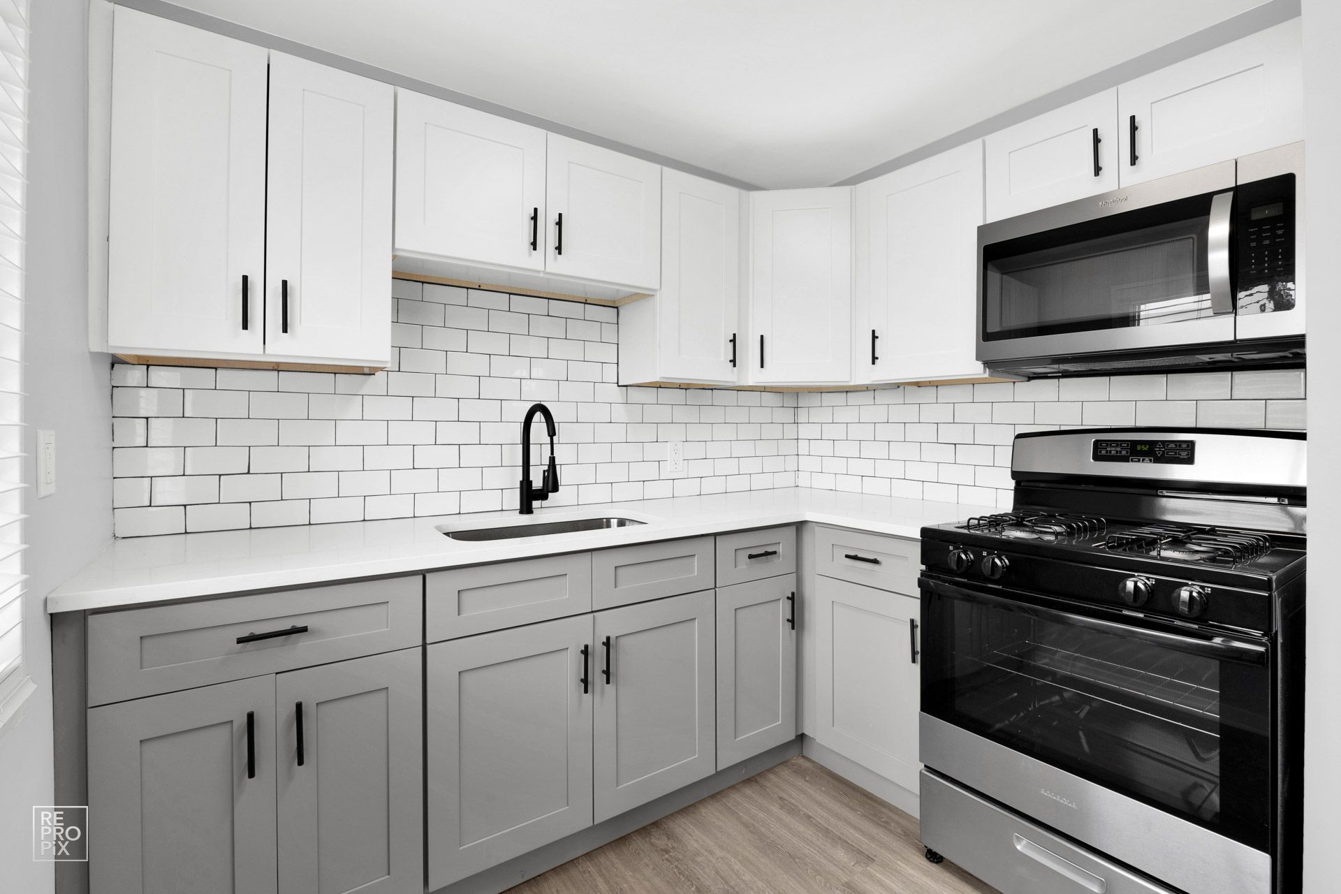 Modern kitchen with gray lower cabinets, white upper cabinets, and stainless steel appliances.