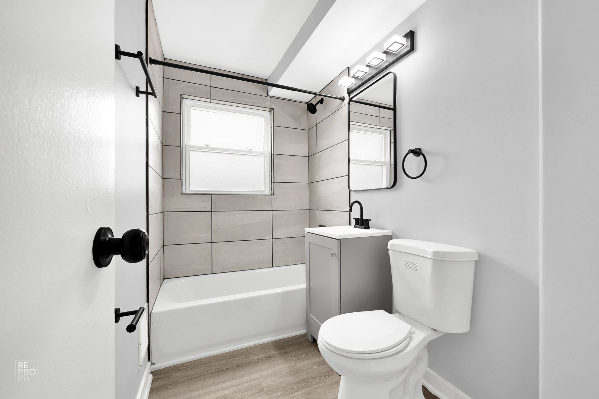 Bathroom with gray walls, bathtub, vanity, and toilet. Black fixtures and white trim.