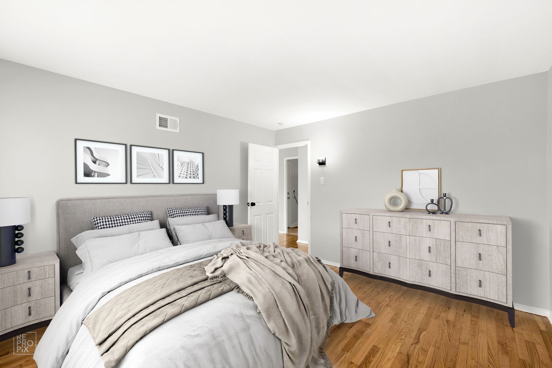 Bedroom with a gray upholstered bed, light wood dresser, and framed artwork.