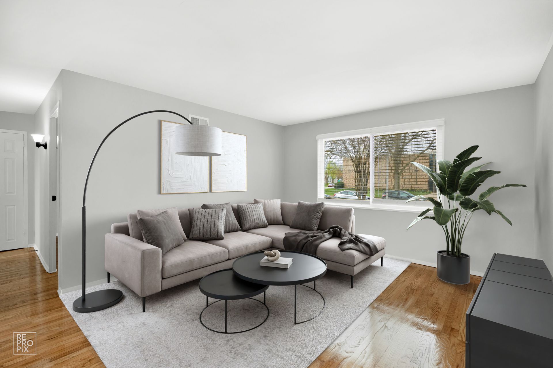 Living room with a sectional sofa, coffee table, and large arched lamp; window with trees outside.