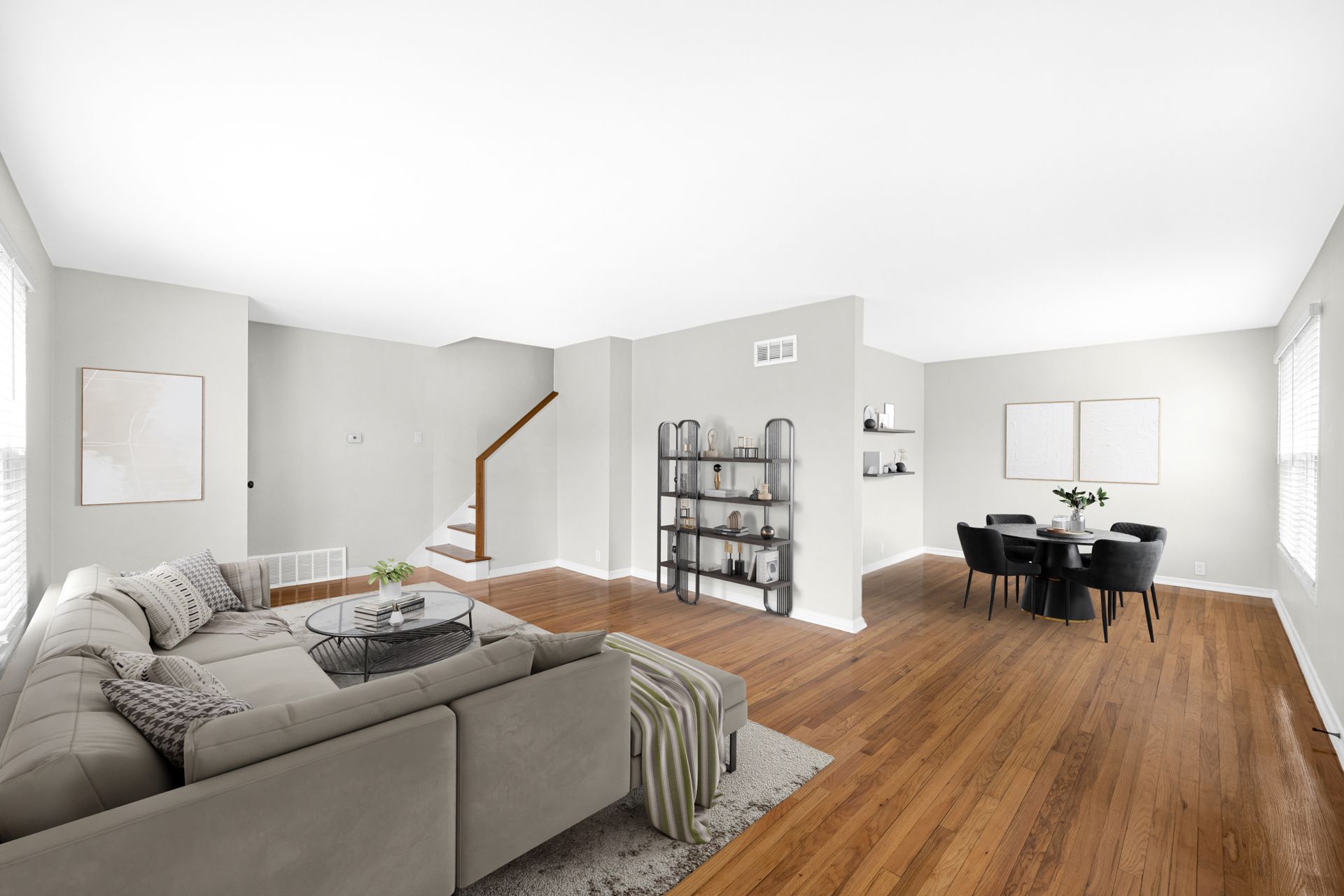 Open-concept living space with a sectional sofa, dining table, and staircase; hardwood floors and neutral walls.