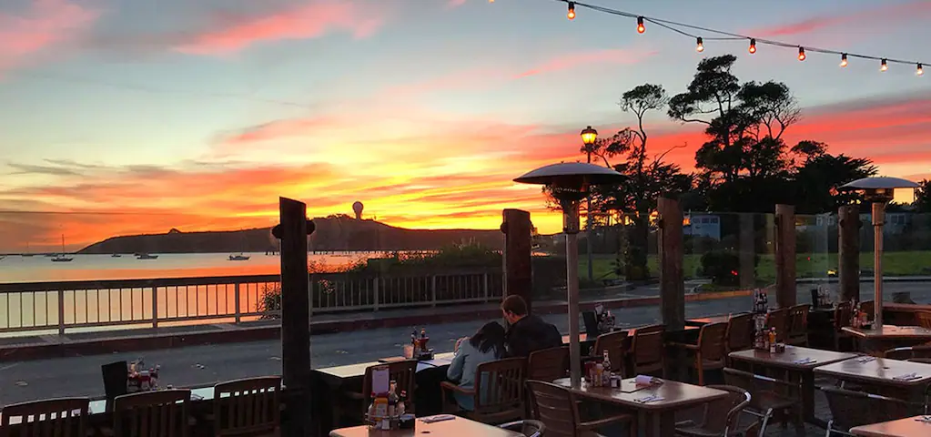 A couple sitting at the table outside at Half Moon Bay Brewing Company enjoying the sunset and the view at the bay.