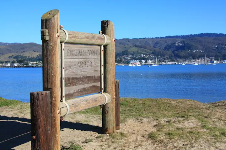 Pillar Point Harbor wooden sign. Bay and boats on the background.