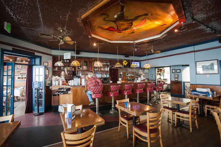 Vintage interior of Moss Beach Distillery: bar with 6 bar red chairs and  6 tables.