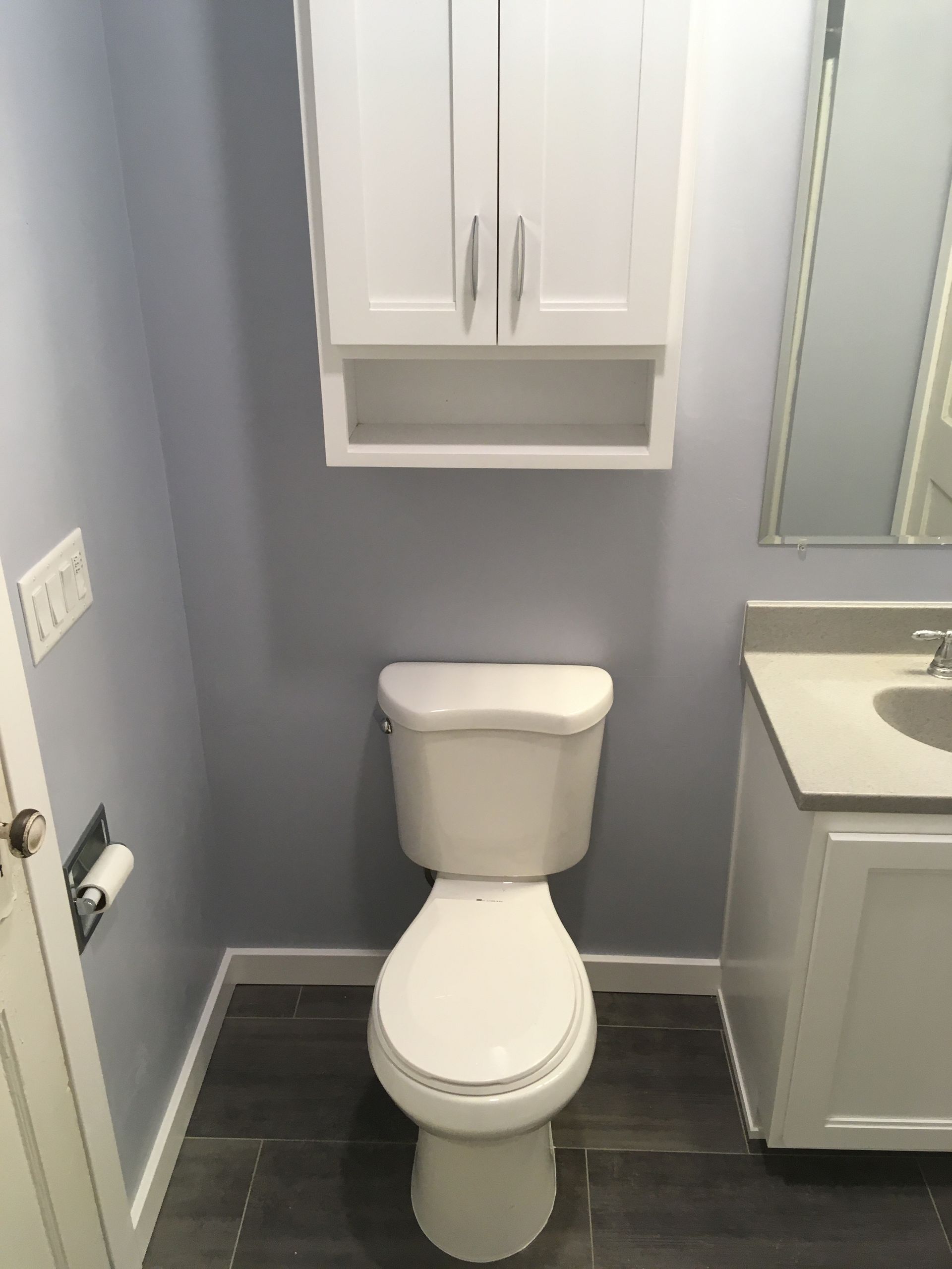 A bathroom with a toilet , sink , cabinet and mirror.